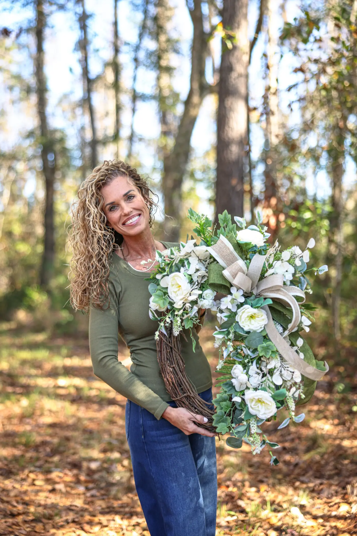 Kandi Jung holding a handmade cream and eucalyptus grapevine wreath outside her Savannah workshop